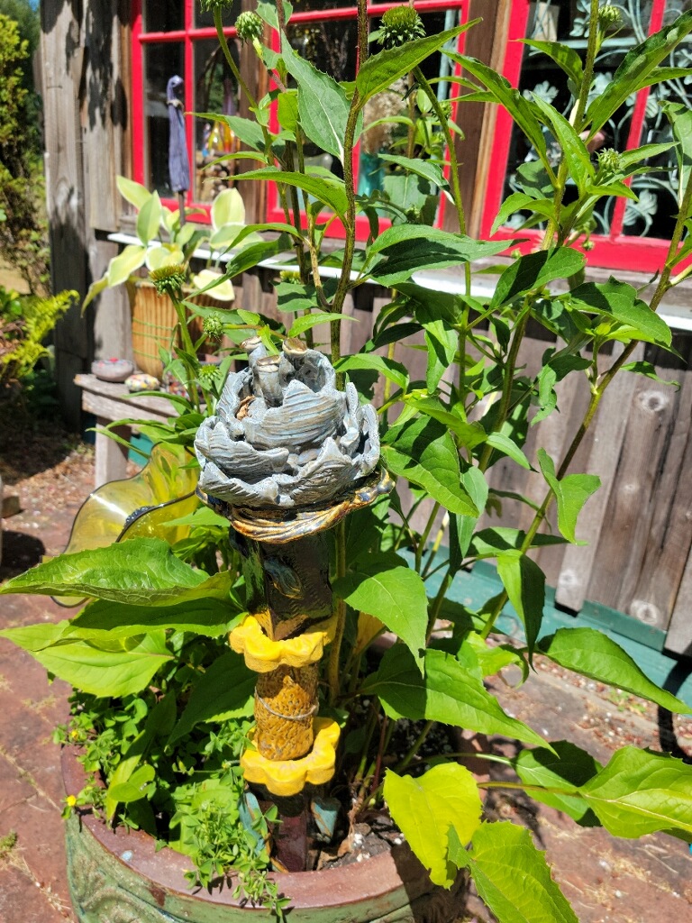 Rustic ceramic totem in a garden pot with green leafed plants