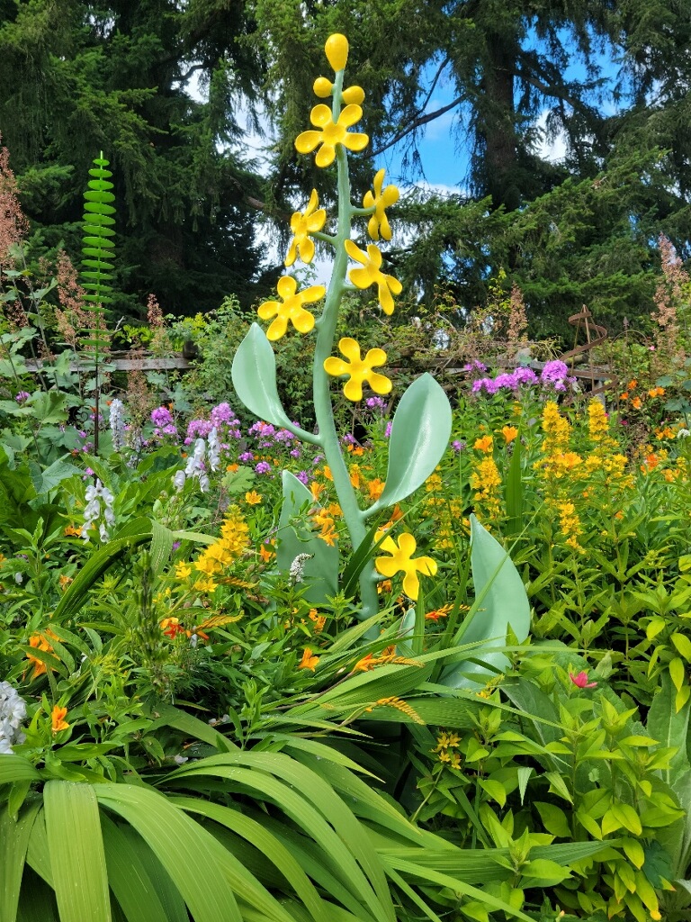 Whimsical stylized yellow flower stock sculpture set among a blooming perennials