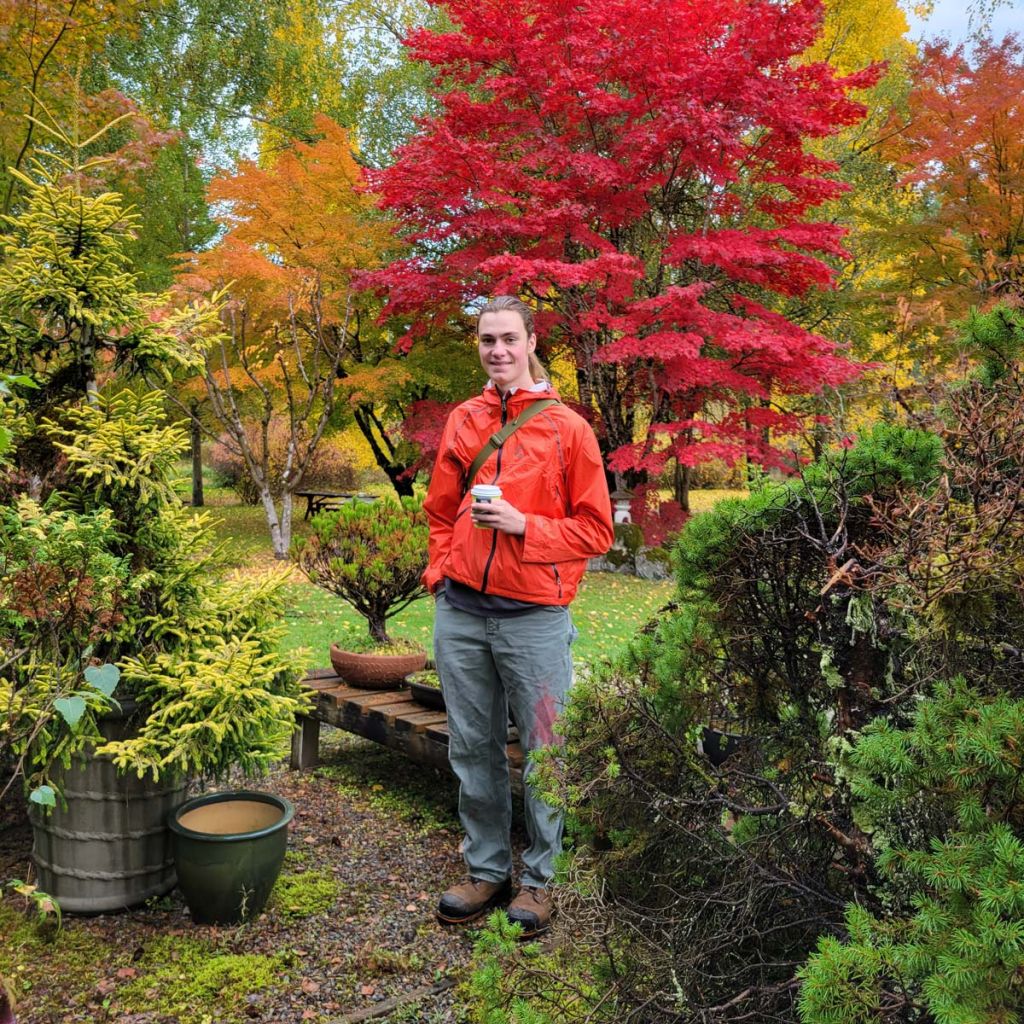 Young man in a fall garden, trees in the background are brightly colored